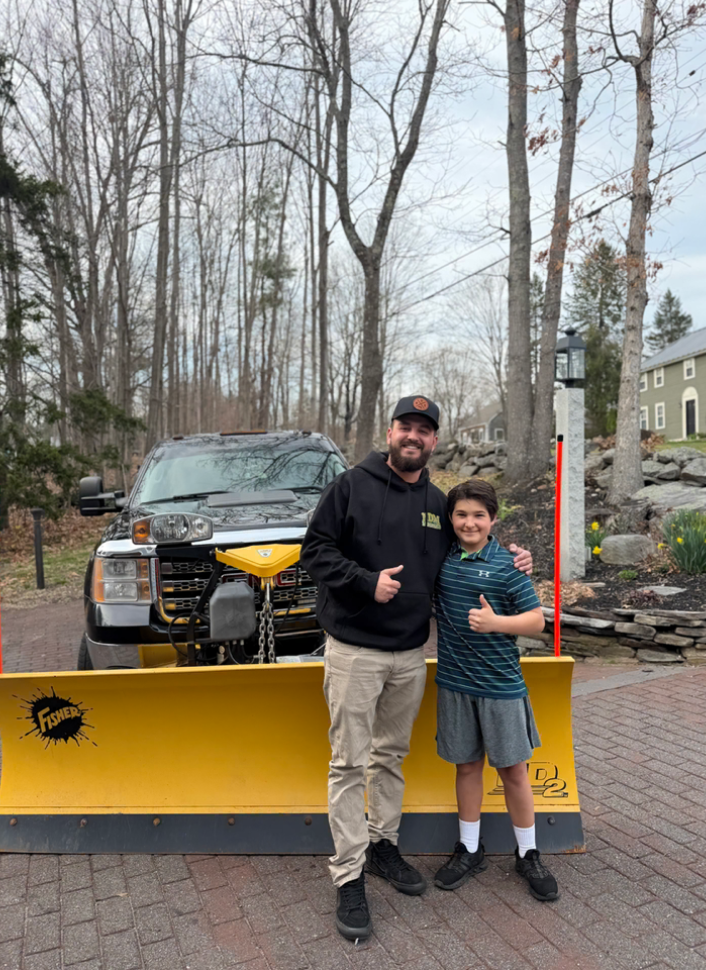 Plows4Seniors team member and young helper standing in front of a plow-equipped truck, giving thumbs up
